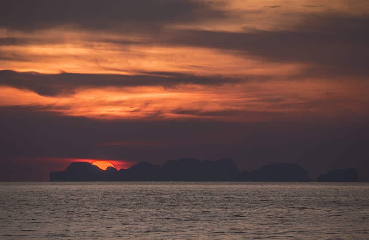 watching an orange sunset fall behind a far away island in the ocean from koh lanta