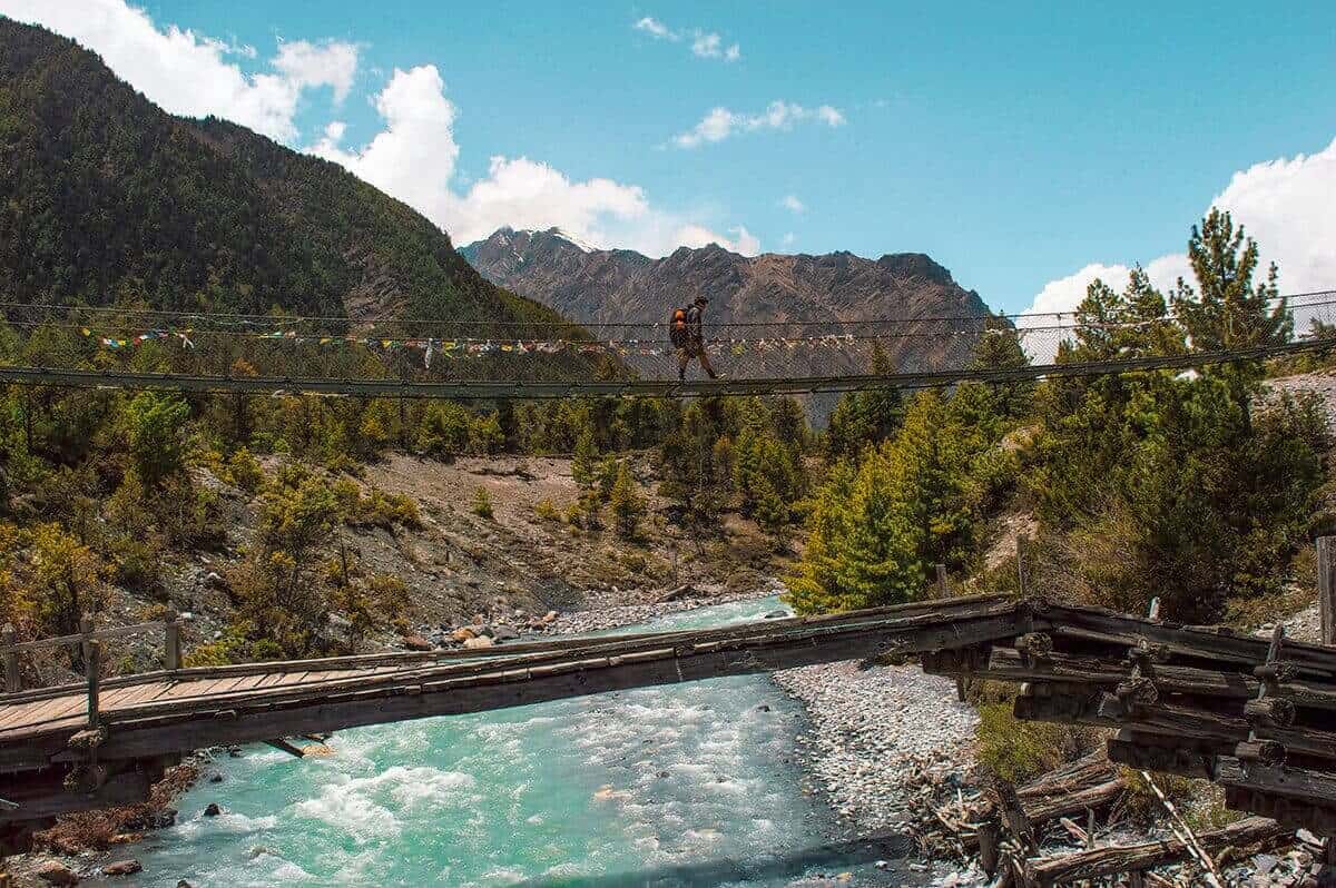 hikiing over a bridge with icy water underneath on the annapurna circuit
