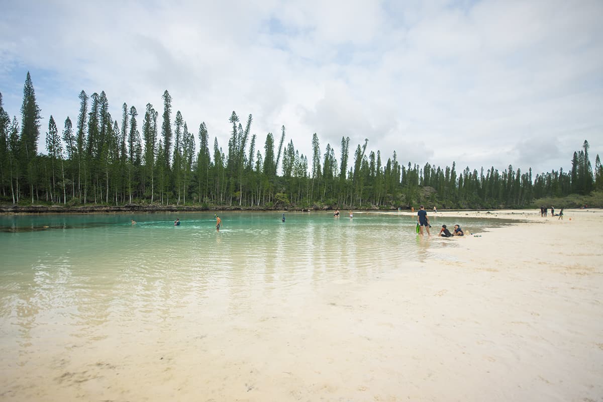 holiday makes and a few cruise goers checking out the natural pool in isle of pines during a low tide and slightly overcast day