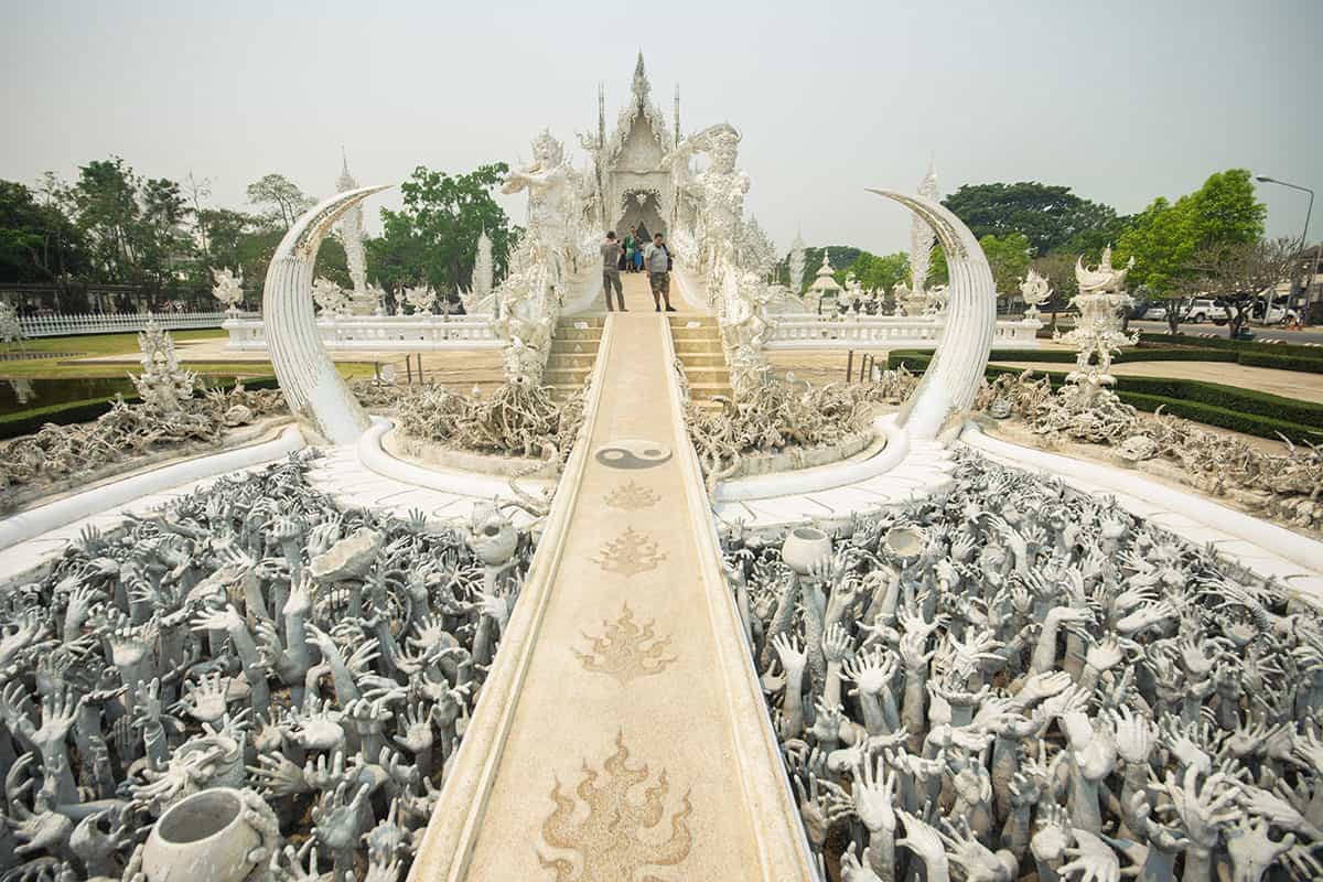 hands reaching out over the bridge at the white temple in chiang rai