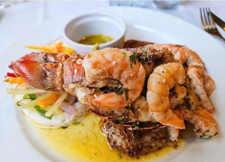 Best Restaurants In San Pedro Belize For Breakfast, Lunch & Dinner 19 A beautifully plated surf and turf meal at hidden Treasure Restaurant in San Pedro Belize, displaying succulent grilled shrimp atop a juicy steak with a side of butter sauce, inviting diners to one of the renowned restaurants in San Pedro Belize for seafood and meat lovers alike.