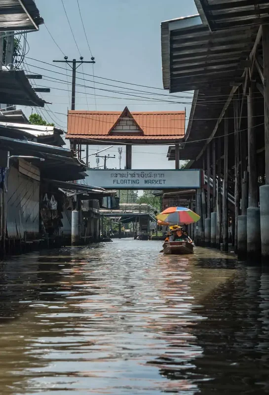 looking down one of the canals to the bridge with the sign floating market in bangkok