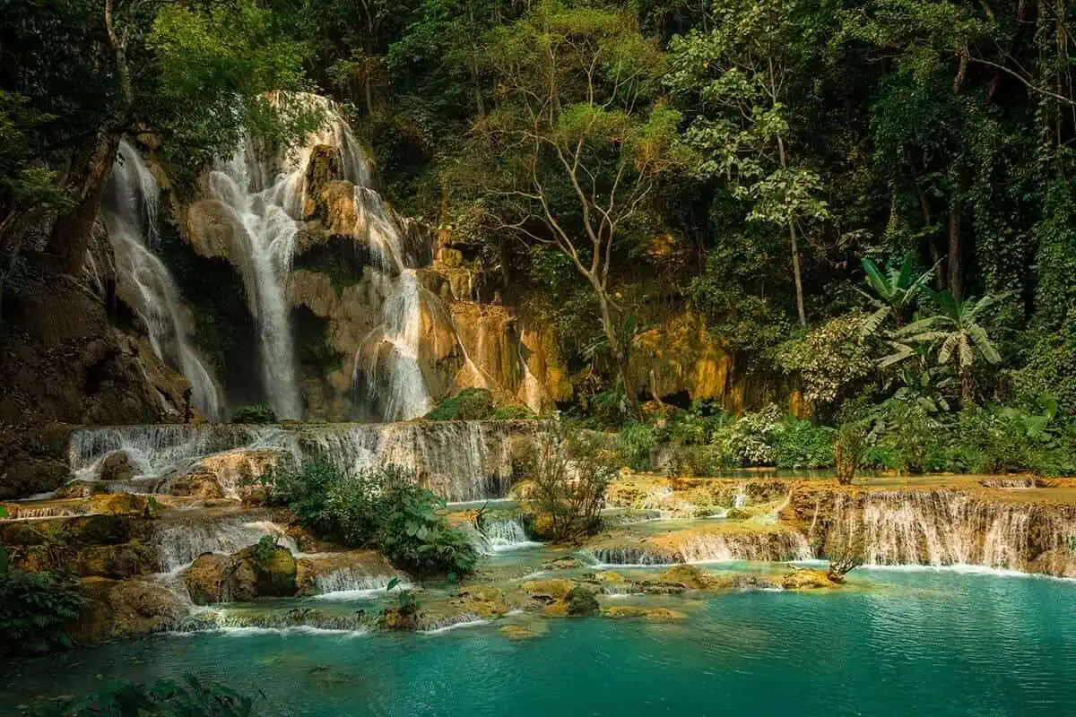 the main waterfall at kuang si falls surrounded by liush jungle