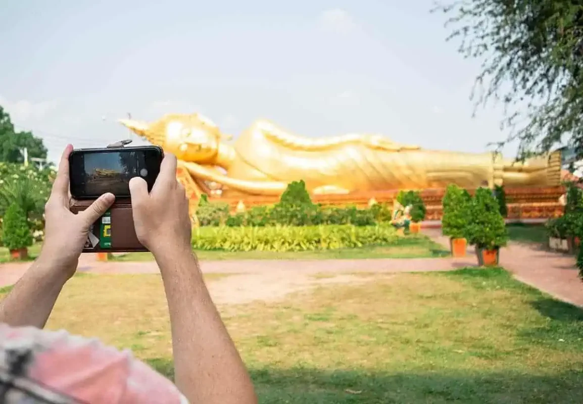 a person taking a photo of his phone of the golden reclining buddha in vientiane