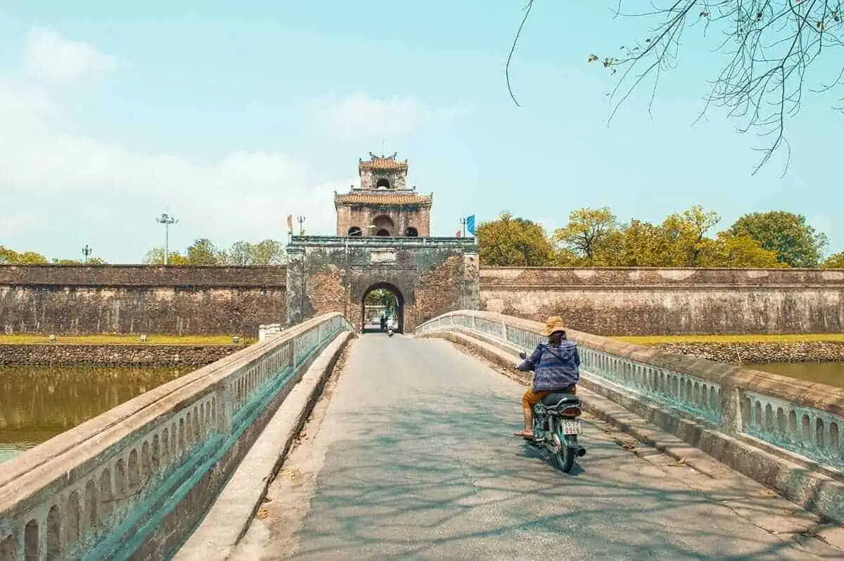 Motorcyclist crossing an ancient bridge leading to a historic gate in Hue, a cultural highlight for 3 weeks in Vietnam.