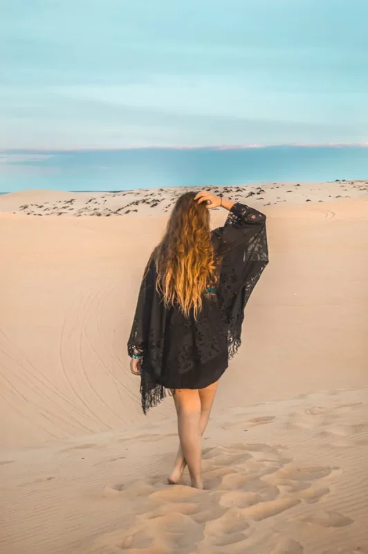 tasha amy in a black shawl walking on the sandy dunes with footsteps behind her, a serene moment in a 3 week Vietnam adventure.