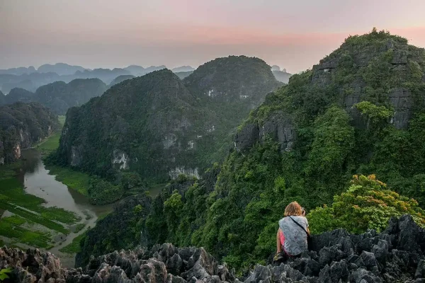 A traveler sitting atop rugged karst peaks overlooking the river in a valley on the ultimate 3 weeks in Vietnam itinerary