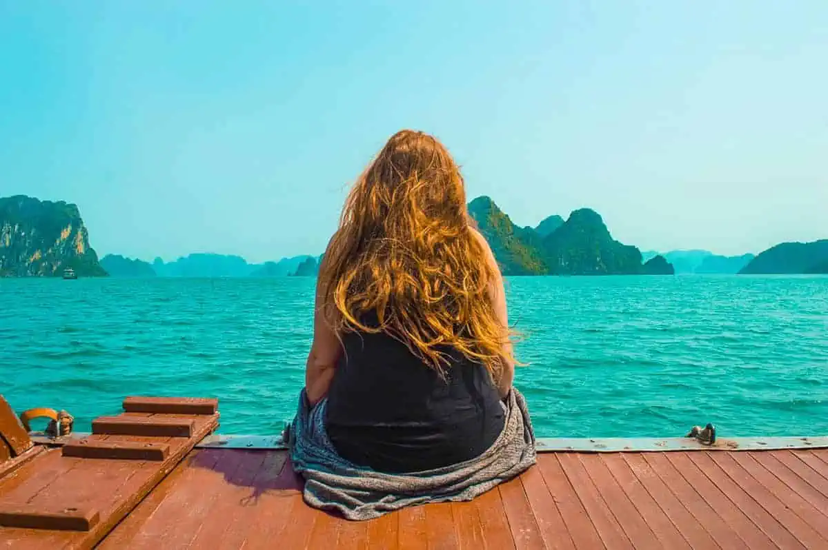 Woman sitting on a boat deck, admiring limestone cliffs emerging from the sea, a peaceful moment to savor on a 3 weeks in Vietnam journey.