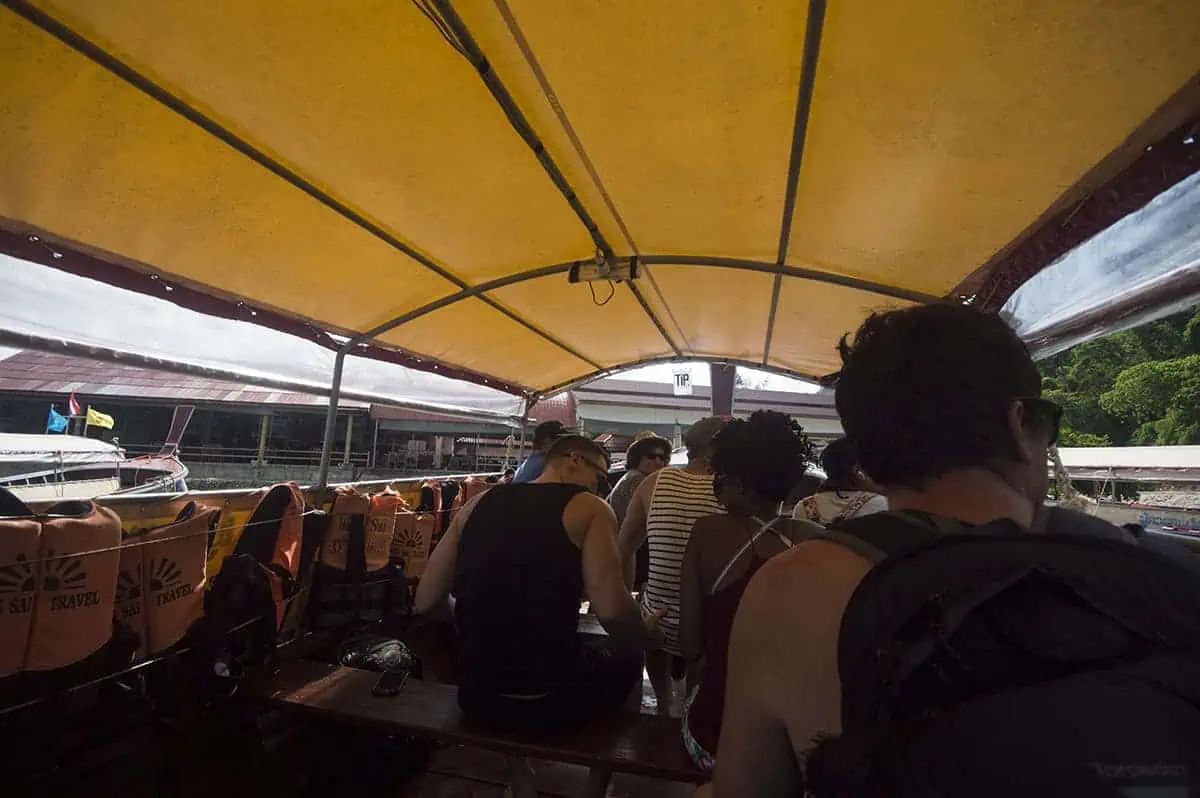 Ao Nang To Railay Beach: The ULTIMATE Guide 2025 6 Passengers sitting under a yellow canopy on a longtail boat preparing to depart from Ao Nang to Railay Beach.