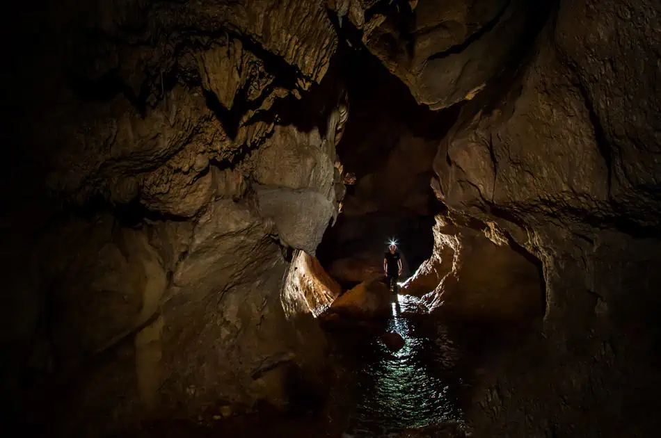 a lone traveler looking out into the atm cave with a head torch on