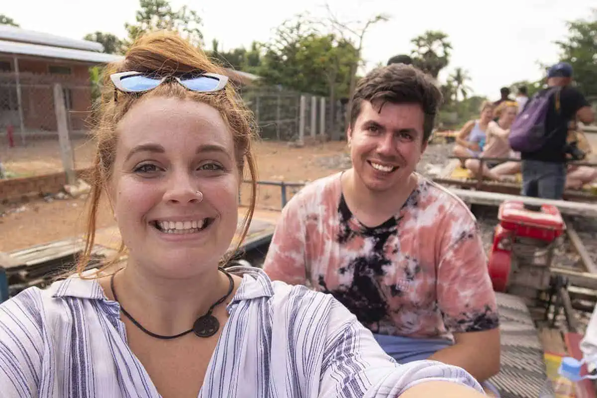 tasha amy takes a selfie on a bamboo train in Battambang. In the background is some other travelers and a few carts.