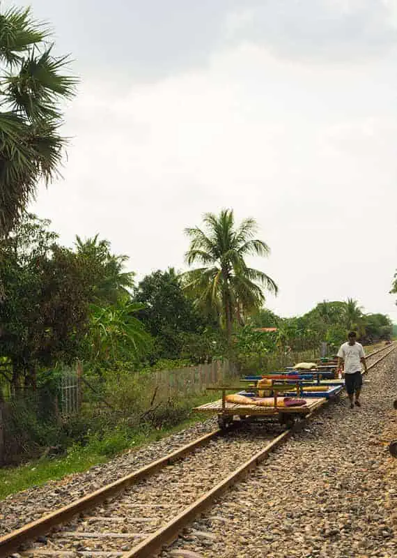 A man walks alongside several bamboo train platforms lined up on an old railway track, setting them up for groups to jump on.