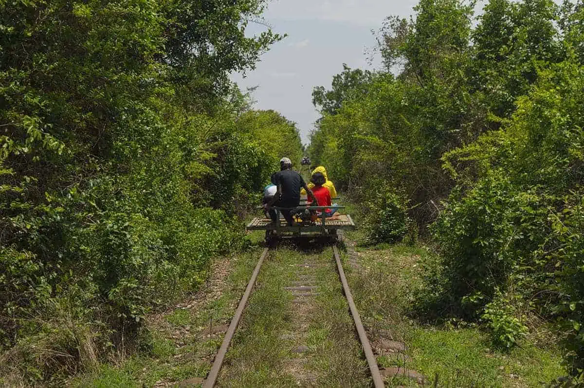 the old bamboo train in 2017 with the overgrown jungle and track. A group ride the a narrow track, with bush forming a tunnel around the rails.