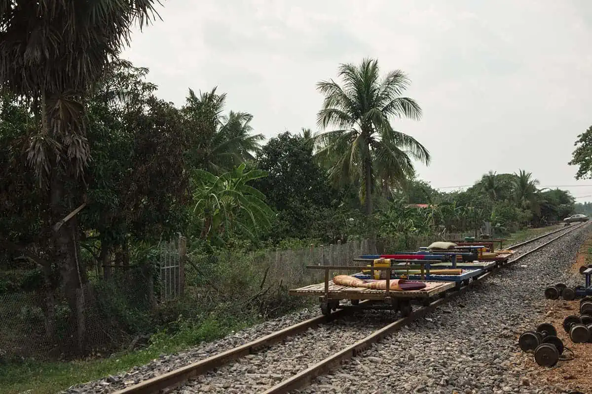 Multiple bamboo trains rest on a railway line, with spare wheels on the ground.