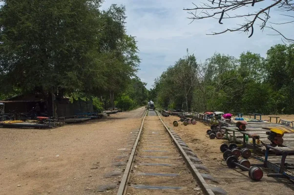 A straight view down the Battambang bamboo train tracks, with rows of dismantled train carts and wheels resting on both sides of the rail line.