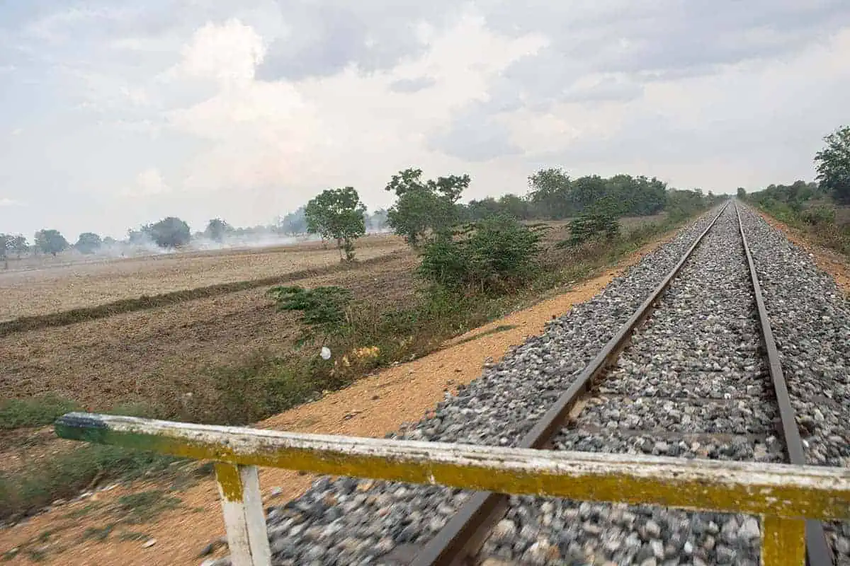 View from the battambang bamboo train looking down a long stretch of rocky rail track cutting through dry Cambodian farmland.
