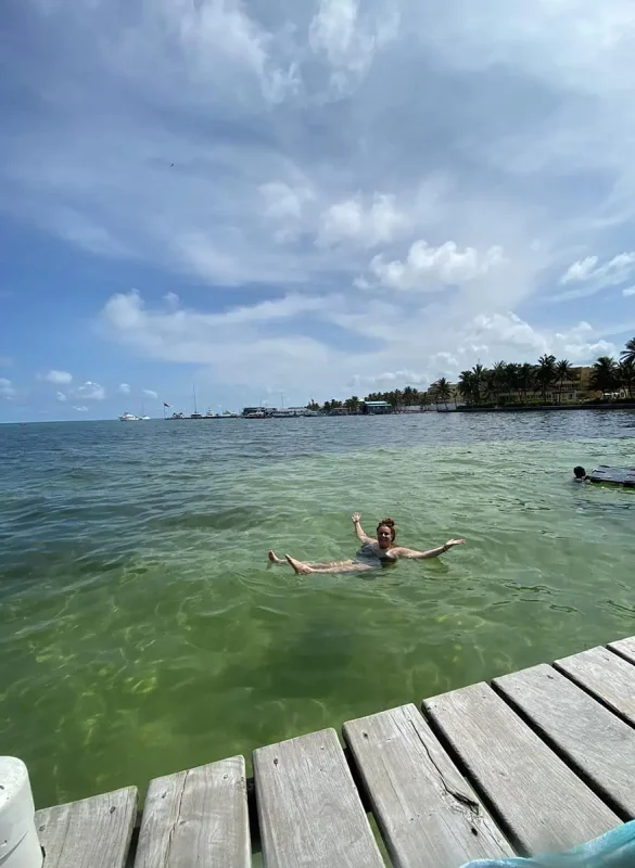 Belize In June: Is Belize Worth Visiting In June? 22 Tasha Amy floating joyfully in the clear turquoise waters off a wooden dock in Belize, showcasing the leisure activities available in the sunny month of June.
