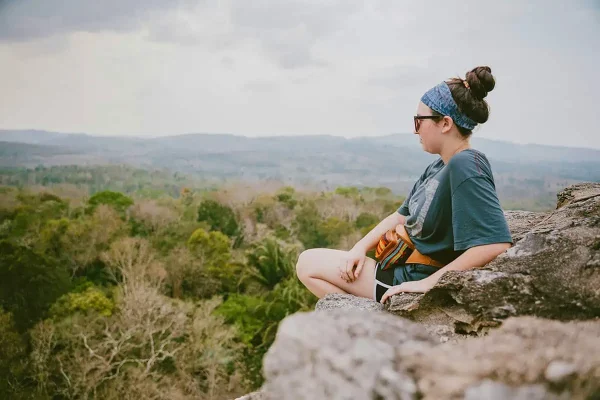A serene moment captured as a person sits atop a rocky outcrop, gazing across the vast jungle landscape of Belize, perfect for reflective Belize Instagram captions and Belize puns