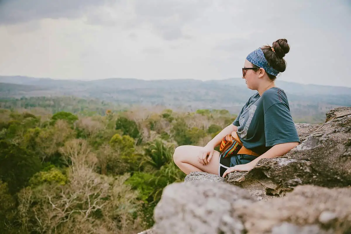 A serene moment captured as a person sits atop a rocky outcrop, gazing across the vast jungle landscape of Belize, perfect for reflective Belize Instagram captions and Belize puns