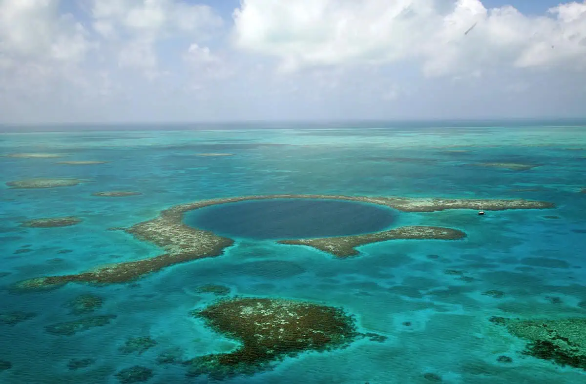 Aerial view of the famous Great Blue Hole at lighthouse atoll in Belize surrounded by shallow coral reefs and a solitary boat near its edge, illustrating the scale and beauty of this natural wonder.