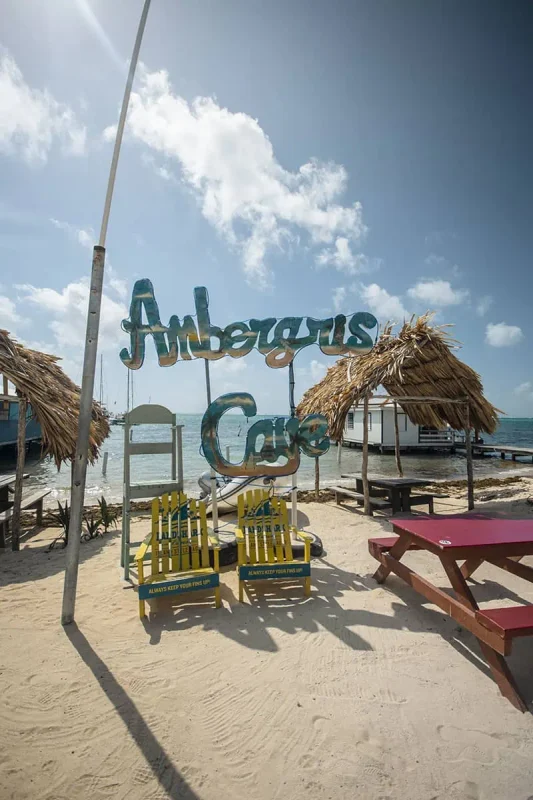 A vibrant sign reading "Ambergris Caye" with a picnic table and thatched structures in the background, depicting a popular spot for tourists to visit on the island.