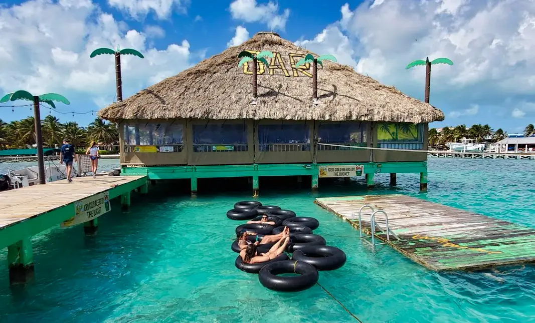 People relaxing on inner tubes next to a floating bar with tropical palm decorations, highlighting the fun and unique water activities available on Ambergris Caye's beaches.