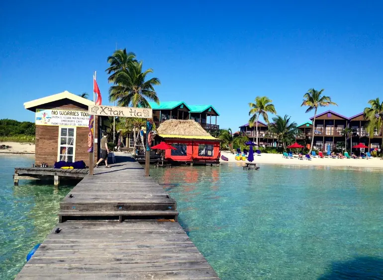 A wooden pier leading to vibrant beachfront businesses and palm trees, with the calm sea inviting visitors to explore the best beaches in Ambergris Caye.