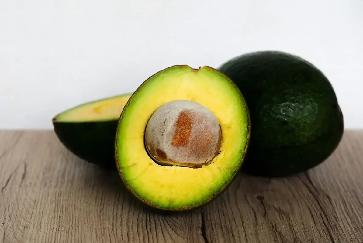 A halved avocado with a rich, creamy texture and a large brown pit, presented on a wooden surface.