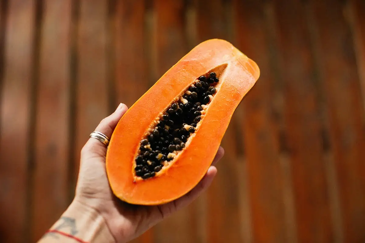 Hand holding a half-cut ripe papaya with black seeds, highlighting the vibrant orange flesh of this tropical fruit found in Belize.
