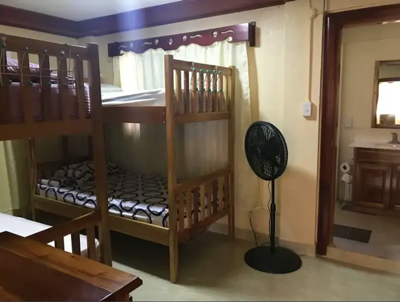 Cozy and well-maintained dormitory room with wooden bunk beds and a standing fan, at D's Hostel, one of San Ignacio's comfortable accommodations.
