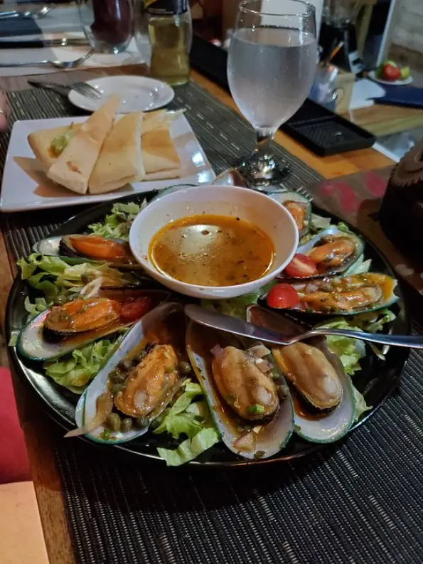 A tantalizing plate of mussels in a garlic broth with fresh greens and toasted bread on the side from crave house of flavors, a must-try dish in San Ignacio's dining scene.