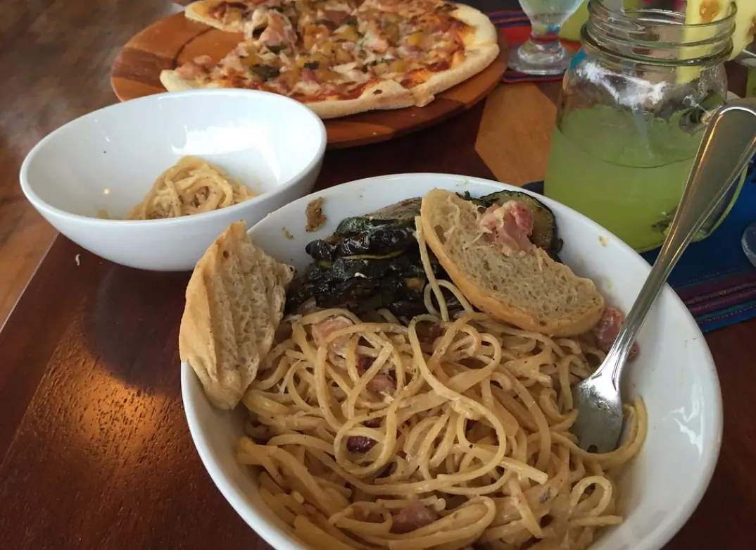 A laid-back meal setting with pasta, grilled vegetables, and a pizza in the background, typical of the relaxed dining atmosphere in guava limb cafe, one of the best restaurants in san ignacio