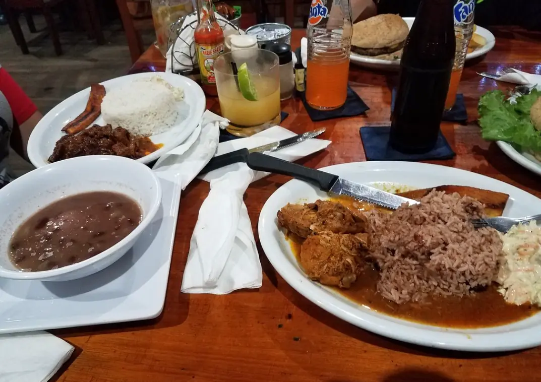 A traditional Belizean meal with stewed meat, rice, beans, and fried plantain, served with refreshing beverages, at ko-ox han nah, a popular eatery in San Ignacio.
