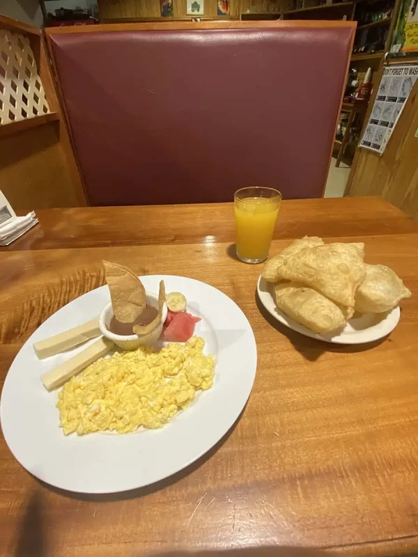 Simple yet satisfying breakfast consisting of scrambled eggs, cheese, ham, and fried jackfruit, served with orange juice, from pops belize restaurant. a common find in San Ignacio's cafes.