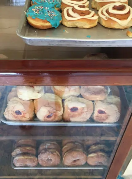 A glass bakery display case filled with a variety of sweet baked goods, including frosted cookies and rolls, in Caye Caulker bakery. The variety and appeal of these desserts highlight the island's culinary delights.