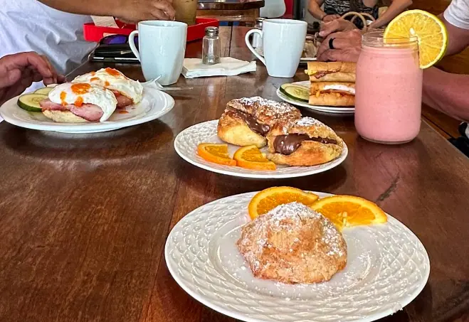 Best Restaurants In San Pedro Belize For Breakfast, Lunch & Dinner 5 A hearty and inviting breakfast from The Baker in San Pedro Belize, featuring eggs benedict with avocado on a toasted English muffin, assorted sweet pastries, and a fresh strawberry smoothie, capturing the essence of the cozy and satisfying morning meals for those searching for where to eat in San Pedro Belize.