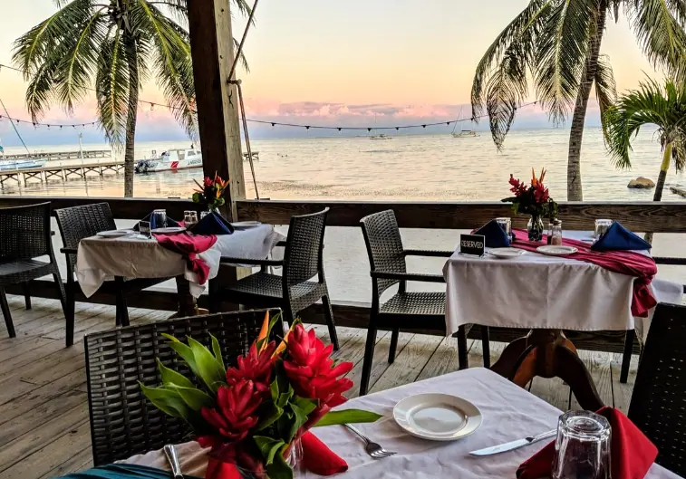 Best Restaurants In San Pedro Belize For Breakfast, Lunch & Dinner 14 The tranquil dining setting of Blue Water Grill in San Pedro Belize, with elegantly set tables on an open-air deck overlooking the serene blue ocean at sunset, offering an idyllic dining experience for those seeking exceptional restaurants in San Pedro Belize.