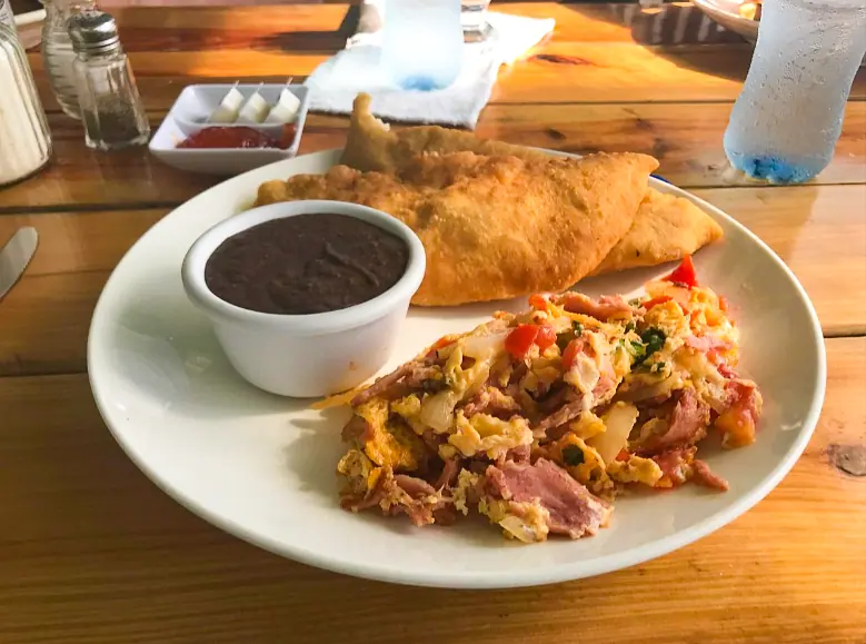 Best Restaurants In San Pedro Belize For Breakfast, Lunch & Dinner 4 A traditional Belizean breakfast plate from Estel’s Dine by the Sea, featuring a hearty helping of scrambled eggs with ham and veggies, served with a side of fry jacks and black beans, a favorite among the breakfast spots in San Pedro Belize.