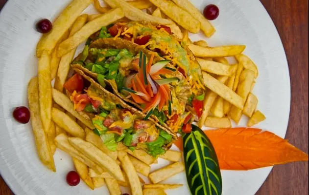 A savory chicken taco salad surrounded by golden French fries, artfully presented on a white plate, exemplifying the fusion of local flavors with international fare at Pineapples Restaurant, one of the best restaurants in san pedro belize