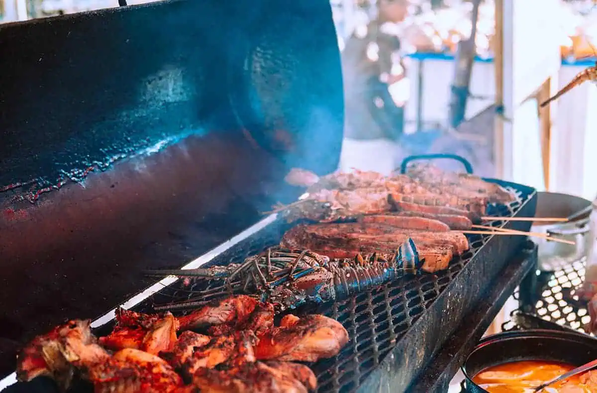 A smoky barbecue grill loaded with various meats, including chicken and lobsters, with skewers of grilled vegetables. The open-air cooking setup adds to the island’s rustic charm. Having a barbecue is one of the best things to do in Caye Caulker, especially with fresh local seafood.