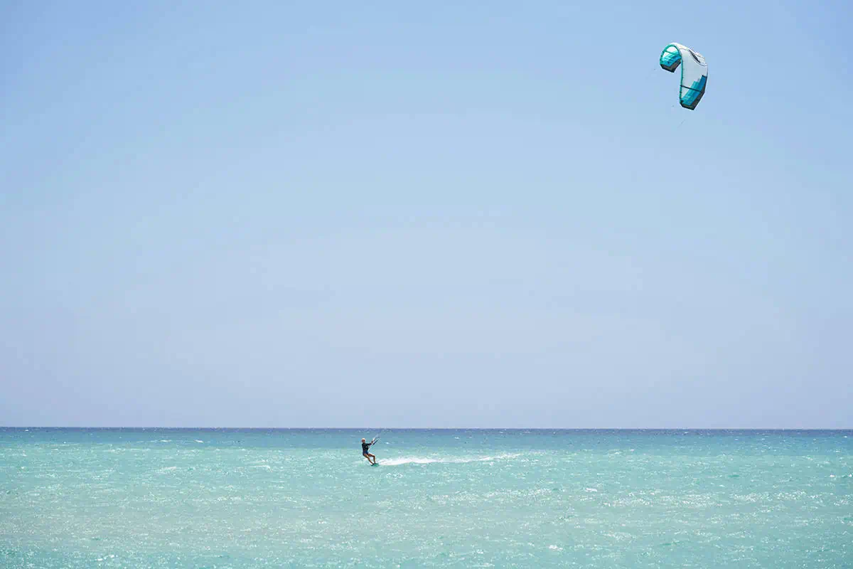 A kite surfer rides the gentle waves off the coast of Ambergris Caye, demonstrating the thrill and fun of one of the island's popular water sports against the backdrop of the clear blue sky.