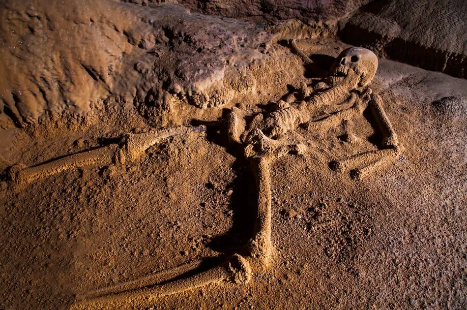 Close-up of an ancient skeleton lying on the sandy ground inside a cave. The bones are partially covered in dust, emphasizing the archaeological significance and the historical explorations that can be undertaken in the caves of San Ignacio.