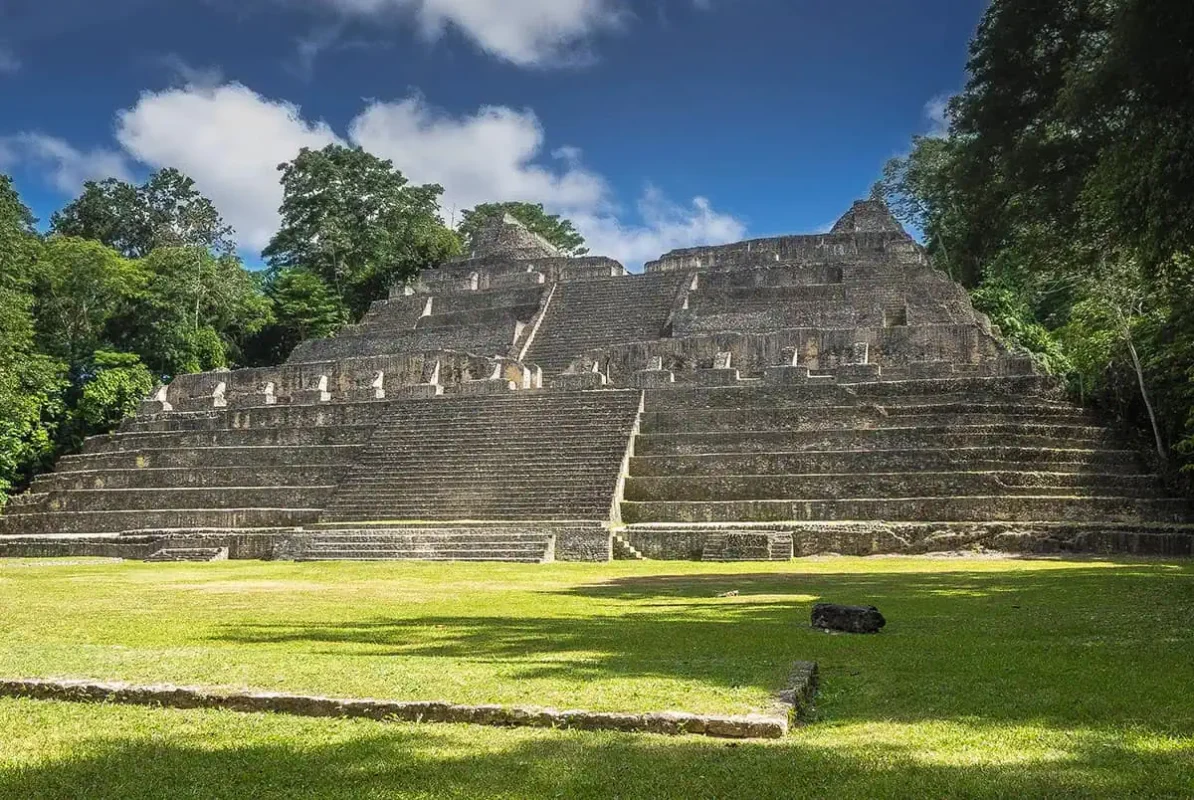 The grand pyramid of Caracol, an impressive Mayan ruin in San Ignacio, Belize. The pyramid features multiple terraces and steep steps, with dense forest greenery providing a striking backdrop against a clear blue sky