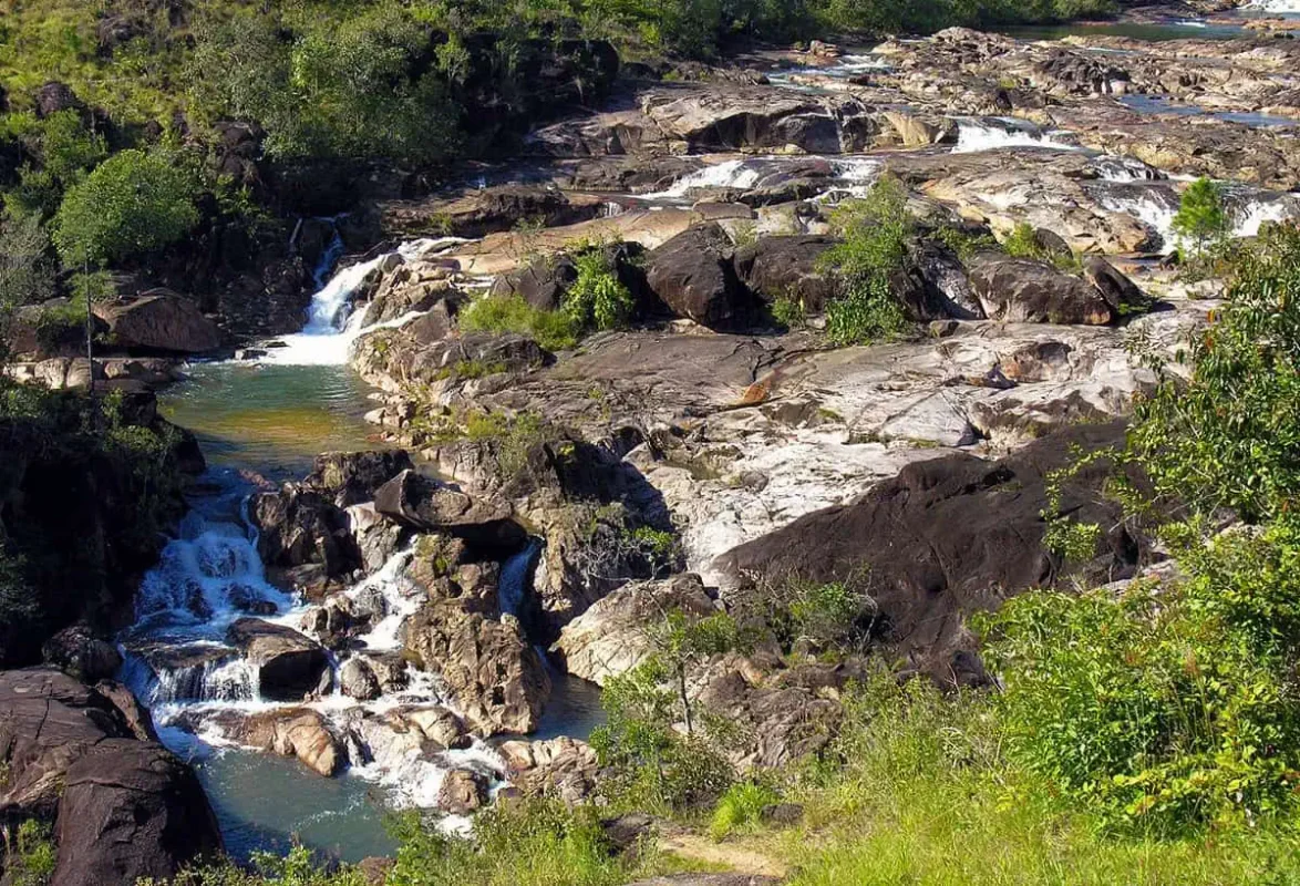 The cascading waters of Rio On Pools in San Ignacio, flowing over smooth rocks and forming natural pools. The surrounding area is lush with green vegetation, offering a serene and picturesque spot for swimming and relaxation.