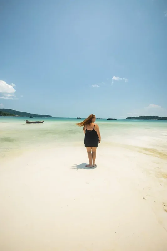 A woman walking on a sandy beach in cambodia, one of the cheapest countries to travel.