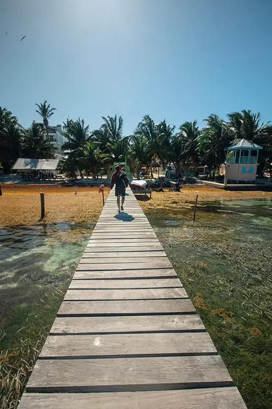 A person walking down a wooden pier near a beach in Caye Caulker.
	