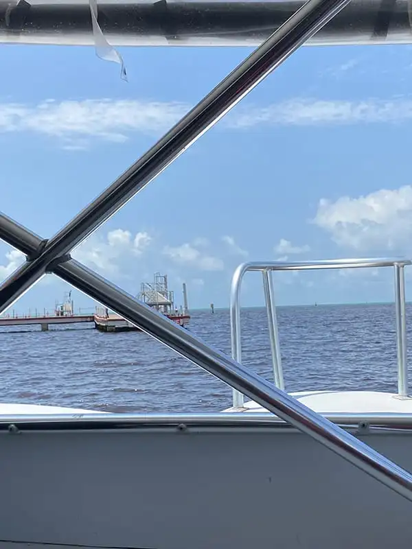 The ocean through the window of a ferry as it departs from Chetumal. The ferry heads across the water, with an industrial port in the distance.