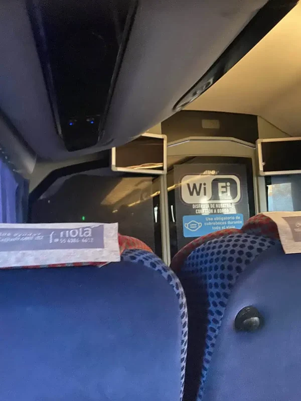 Interior view of an ado bus, showing two front seats and the onboard "Wi-Fi" signage. This bus offers comfortable transportation from Chetumal to Caye Caulker, connecting to the Belize Water Taxi.
