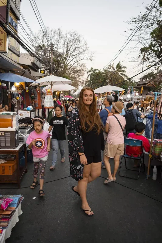 Tasha Amy smiling as she navigates through the bustling lanes of the Sunday Market in Chiang Mai, surrounded by diverse market stalls.