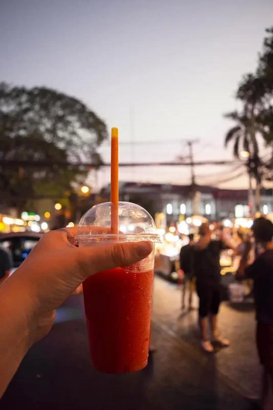 Tasha holding a refreshing a strawberry smoothie with a bustling Sunday market Chiang Mai scene